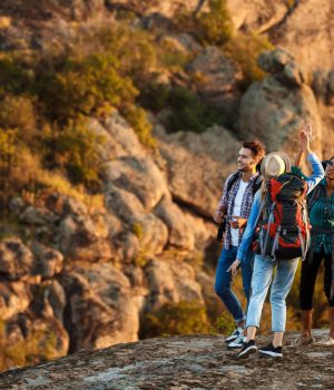 Young cheerful travelers with backpacks smiling, giving highfive, walking in canyon. Copy space.